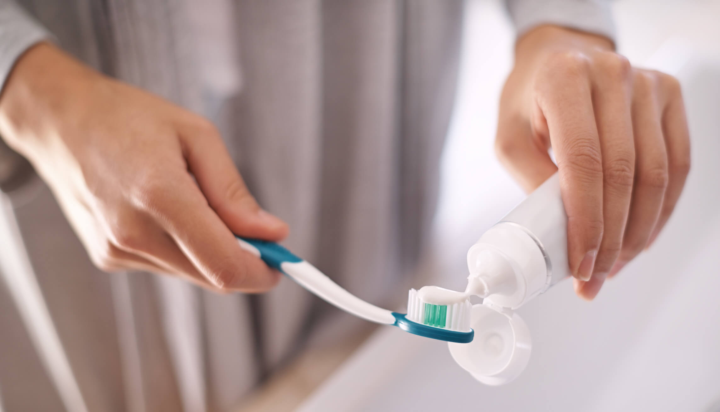 person applying toothpaste to toothbrush