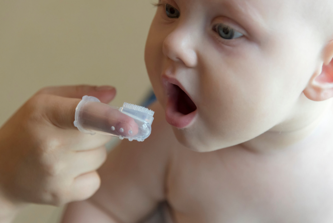 baby's teeth being brushed by plastic brush