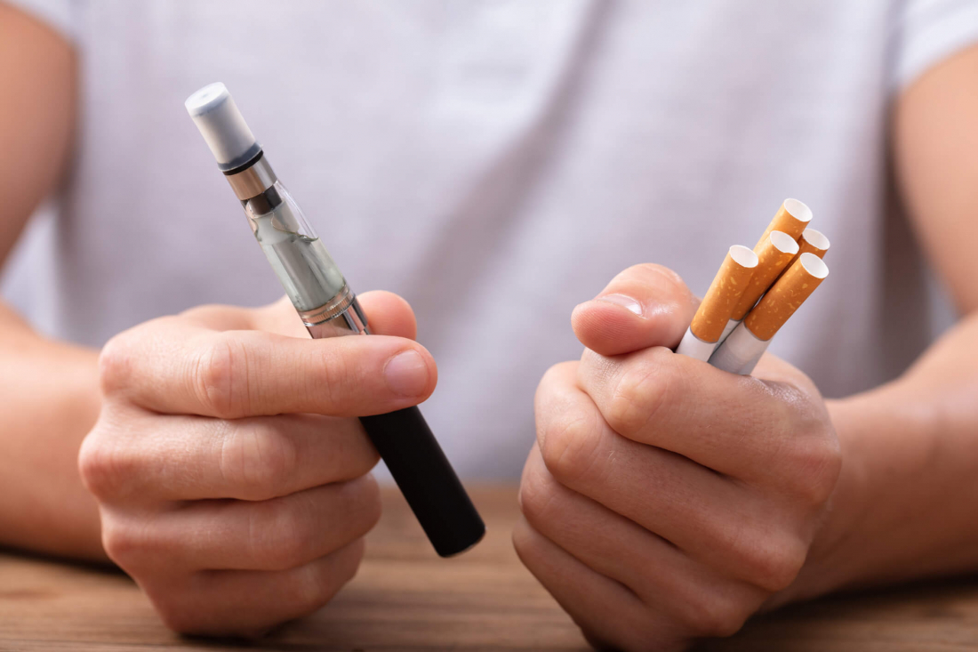 person holding a vape and cigarettes