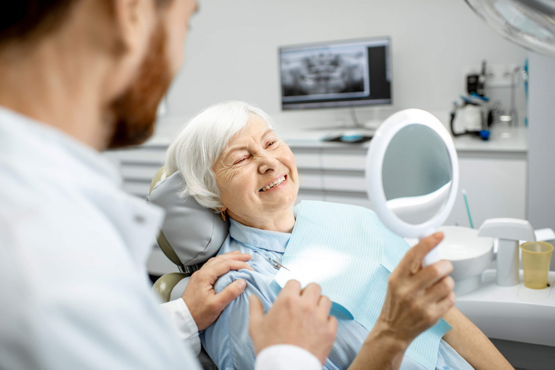 smiling senior woman in dental chair looking in mirror