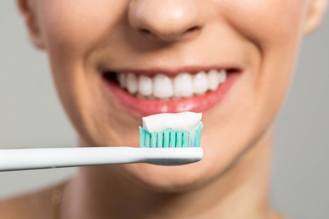 toothbrush with toothpaste on it in front of smiling person