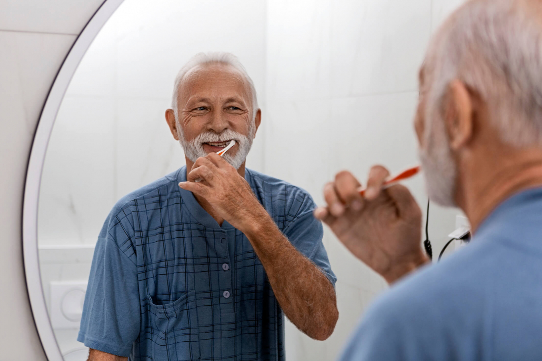 smiling senior man brushing teeth in mirror