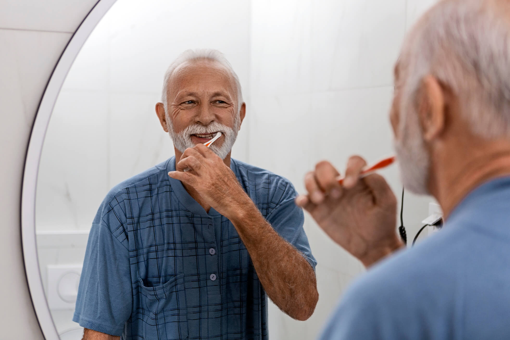 smiling senior man brushing teeth in mirror