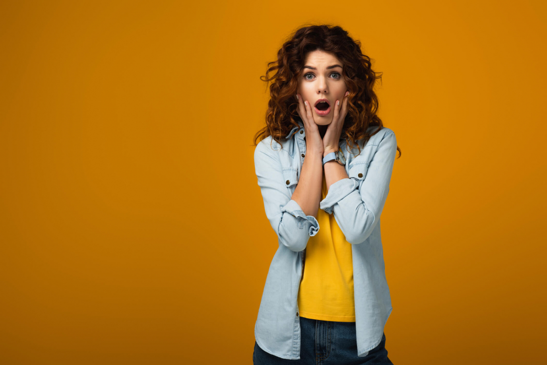 woman with brown hair holding hands on face with mouth open